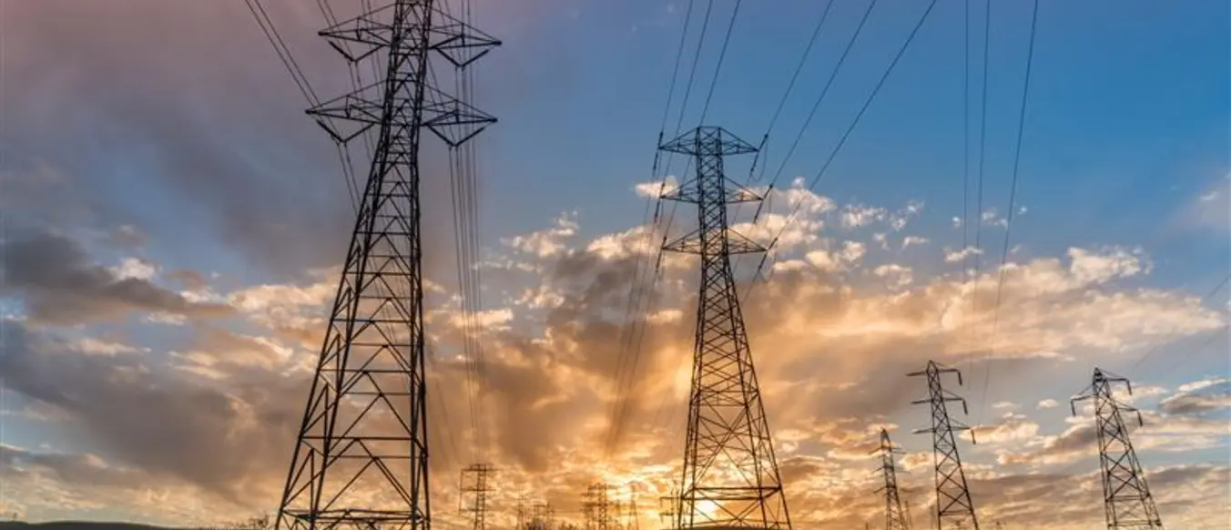 power lines across green field against hills and sunsetting sky