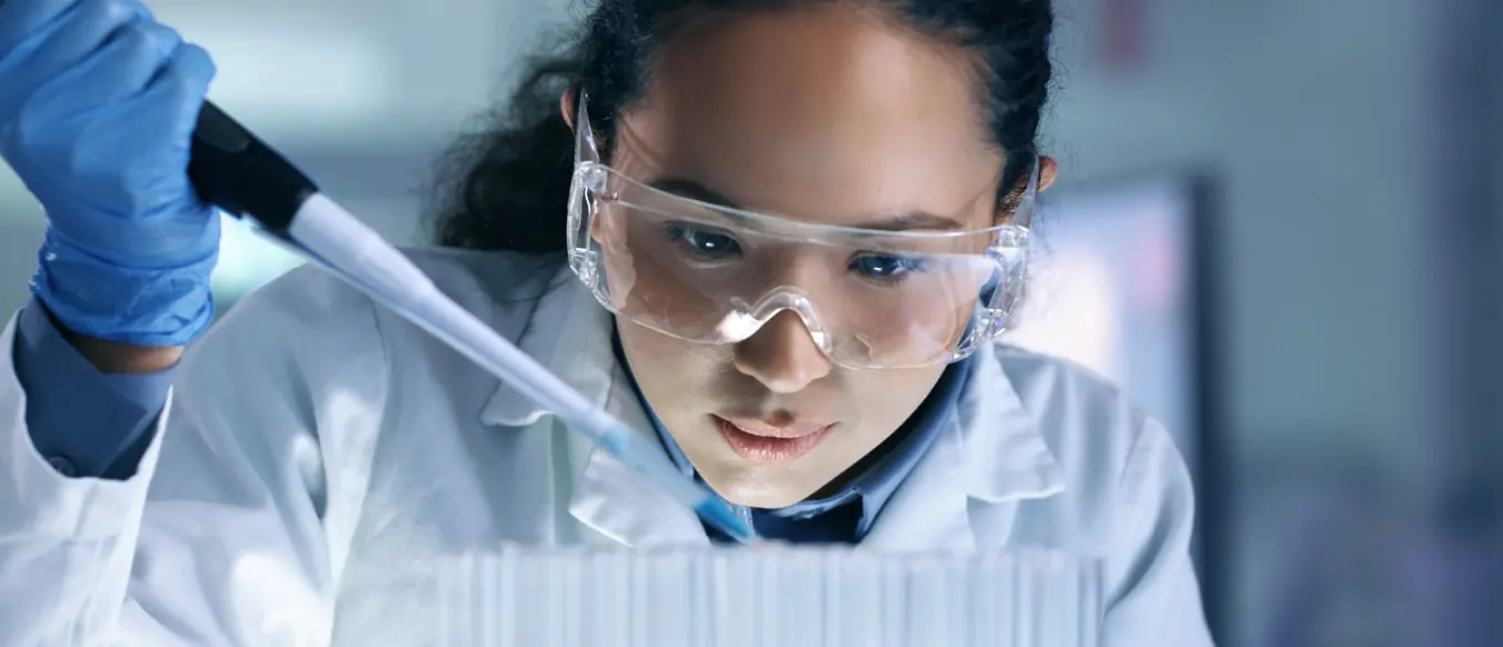 female lab tech in white lab coat with dropper into beaker