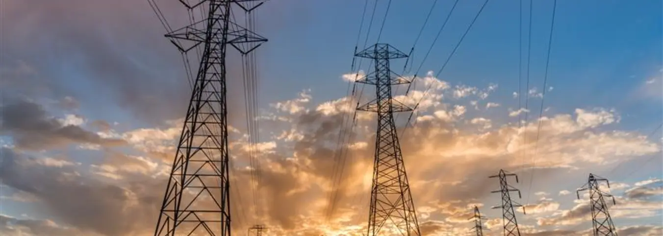 power lines across green field against hills and sunsetting sky
