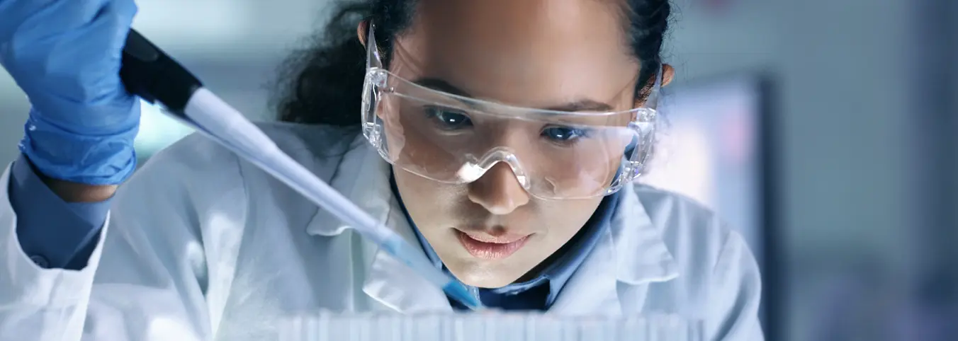 female lab tech in white lab coat with dropper into beaker