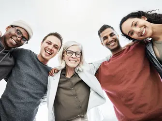 Low angle portrait of team of business people hugging each other. Diverse group of men and women standing in a together in their office, huddling and smiling. Unity and teamwork is key to success
