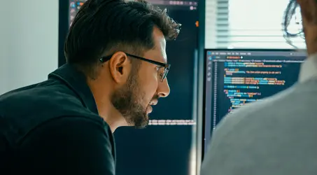Close up of an IT professional reviewing computer code on two computer monitors 
