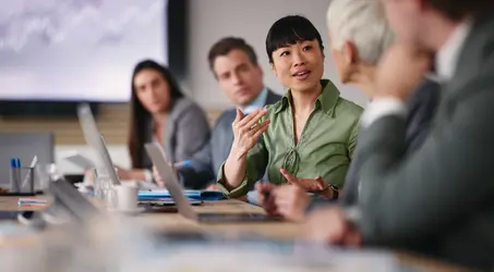 Panel of professionals listening to a woman leading a conversation during a meeting