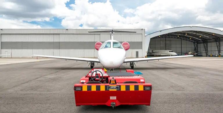 nose of white private jet behind red transport trailer