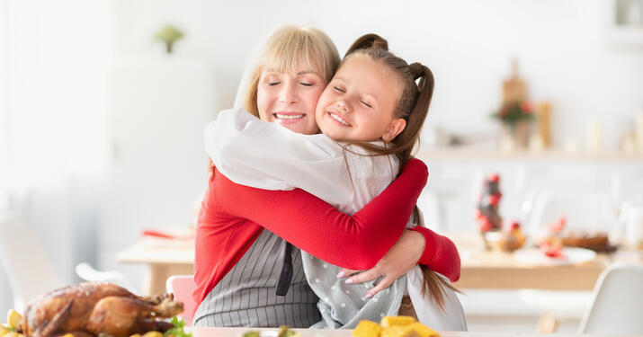 Happy granny hugging granddaughter while cooking traditional holiday turkey for festive family dinner at home