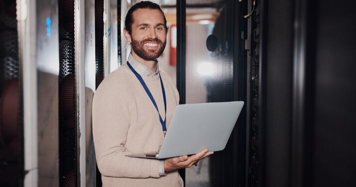 Portrait of a young man using a laptop in a server room at work