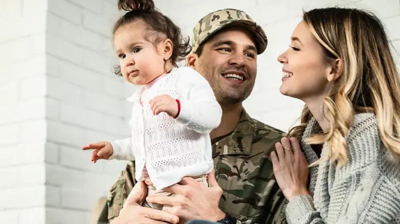 Military family embracing with their baby girl seating on a coach